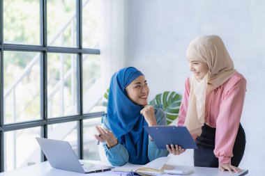 İki modern Müslüman kadın mali grafikler ve dizüstü bilgisayarla toplantı odasında iş görüşmeleri yapıyor ve tartışıyorlar.
