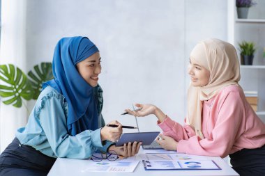 İki modern Müslüman kadın mali grafikler ve dizüstü bilgisayarla toplantı odasında iş görüşmeleri yapıyor ve tartışıyorlar.