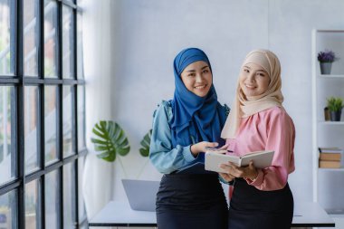 İki modern Müslüman kadın mali grafikler ve dizüstü bilgisayarla toplantı odasında iş görüşmeleri yapıyor ve tartışıyorlar.