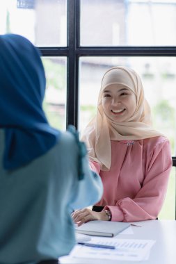 İki modern Müslüman kadın mali grafikler ve dizüstü bilgisayarla toplantı odasında iş görüşmeleri yapıyor ve tartışıyorlar.