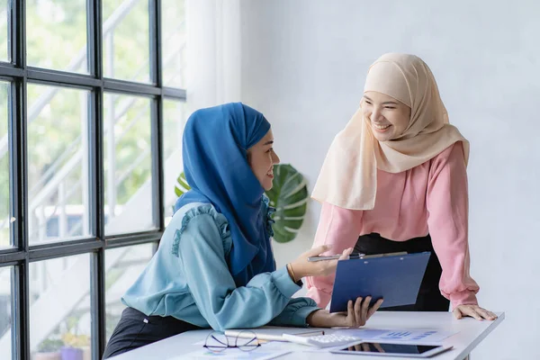 stock image Two young modern muslim women working and discussing work in business meeting at meeting room with financial graphs and laptop