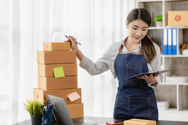 stock image Happy woman selling products online Started as a small SME owner using a laptop computer on a table with parcels of mail in her room.