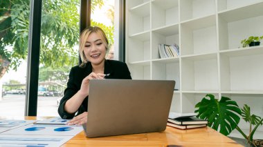 Masada otururken bilgisayarla çalışan iş kadını, evrak işleri, vergi ve mali ekonomi analizi yapan Asyalı iş kadını.
