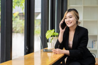 Asyalı iş kadını akıllı telefondan konuşuyor ve bilgisayar ve iş organizasyonu iletişimiyle çevrimiçi çalışıyor.