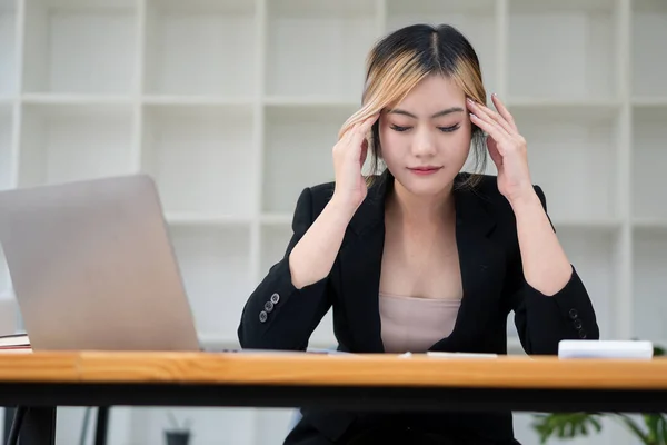 Tired Asian businesswoman Stressed out, headache and strained eyes with heavy work while using laptop computer at work. work overtime