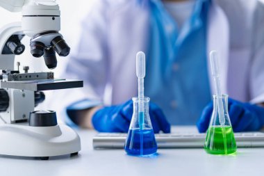 Doktor mavi sıvıyla test tüpü alıyor. Virolog, kimyasal koruyucu giysi üzerinde çalışıyor. Laboratuvar masasında tehlikeli virüs biyoloğu üzerinde çalışıyor.