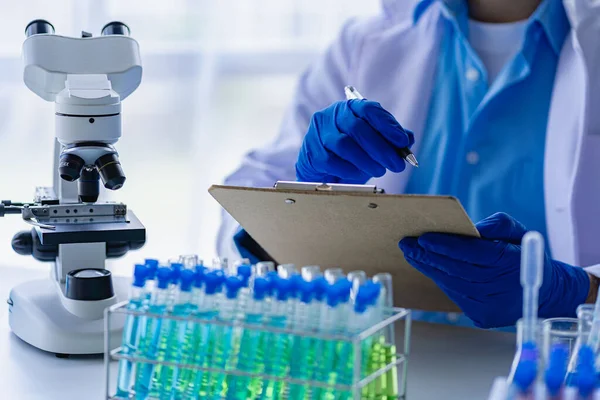 医生用蓝色液体做试管 病毒学家穿上化学防护服 在实验室桌上用显微镜研究危险病毒生物学家 — 图库照片#