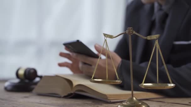 オンライン法的助言および法的助言の弁護士事務所の概念 弁護士が紙のスマートフォンとハンマーでテーブルに座り正義の黄金のスケール — ストック動画