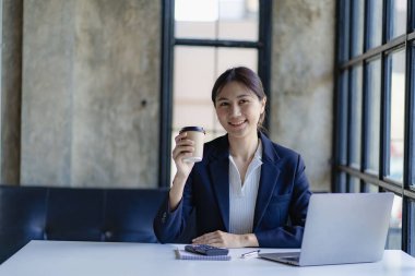 Genç başarılı Asyalı iş kadını akıllı telefon ve dizüstü bilgisayarla müşterilerle iletişime geçmek için çalışıyor, finansal konsept