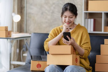 Asyalı kadın internetten sipariş alıyor. Satış, teslimat, pazarlama. Evden çalışırken dijital dizüstü bilgisayarları olan heyecanlı Asyalı genç girişimciler. Küçük işletme Başlangıç KOBİ