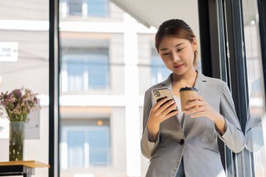 Sosyal medya simgeleri ve sosyal ağları oturma odasında olan cep telefonu kullanan büyük gülümsemeli genç Asyalı kadın..