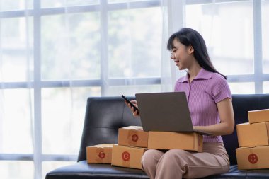 Kanepede oturan ve evde çalışan Asyalı kadın, posta kutusuna internet üzerinden satış ürünleri göndermek için müşteri adresi yazmak için heyecanlı ve gülümsüyor. KOBİ işletme sahipleri kavramı