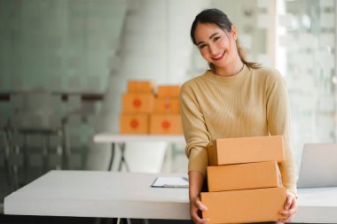 Serbest çalışan Asyalı bir iş kadını bir yığın paket teslimat kutusu tutuyor. Küçük işletme, serbest çalışma ve laptop, bilgisayar, çevrimiçi pazarlama, paketleme kutusu teslim kavramı ile çalışma.