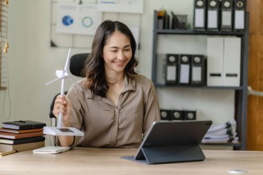 Ofisteki bir tablet bilgisayarın önünde düzenlenen çevrimiçi bir toplantıda rüzgar enerjisi örneklerini ve alternatif enerji tavsiyelerini taklit eden Asyalı bir kadın.