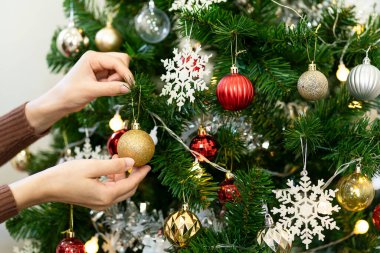 Noel ağacını süsleyen, kırmızı fiyonklu Noel ağacıyla süsleyen bir kadının el resmi ve şenlik süsleme odasında bir hediye kutusu. Mutlu Noeller.