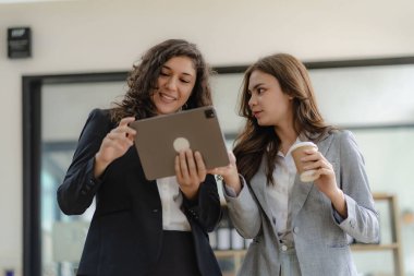 Beyaz tenli genç patron ve asistanı, ofis masasındaki grafik kağıdı ve tablet dizüstü bilgisayara danışmanlık yapıyor.