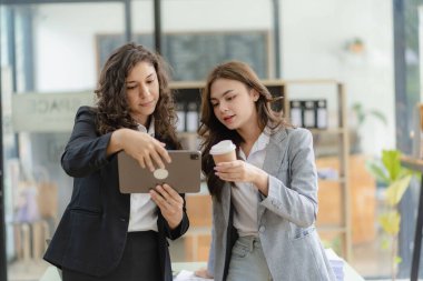 Beyaz tenli genç patron ve asistanı, ofis masasındaki grafik kağıdı ve tablet dizüstü bilgisayara danışmanlık yapıyor.