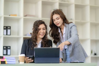 Beyaz tenli genç patron ve asistanı, ofis masasındaki grafik kağıdı ve tablet dizüstü bilgisayara danışmanlık yapıyor.