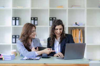 Beyaz tenli genç patron ve asistanı, ofis masasındaki grafik kağıdı ve tablet dizüstü bilgisayara danışmanlık yapıyor.