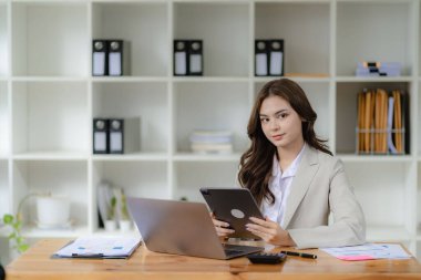 Finansal muhasebede çalışan kadın muhasebeci çizelgeleri analiz ediyor bilgisayarlı hesap makinesiyle belgelerini hazırlıyor ve elinde kahve bardağıyla emlak ofisinde kalem tutuyor.