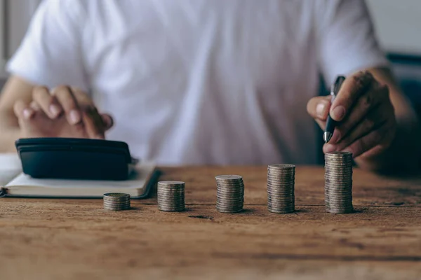 Asian man calculating finances about future expenses or investments at home While the coins are arranged like a graph ahead of the concept of Savings and accounts