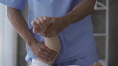 Genç bir adam, erkek bir hastaya rehabilitasyon kliniğinde yardım eden bir fizyoterapist ve yaralanma rehabilitasyonu ile fizik tedavi görüyor. Yüksek kalite 4k video.