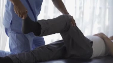Genç bir adam, erkek bir hastaya rehabilitasyon kliniğinde yardım eden bir fizyoterapist ve yaralanma rehabilitasyonu ile fizik tedavi görüyor. Yüksek kalite 4k video.