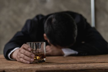 Alkolizm konsepti. Genç adam çok fazla alkol içiyor. Stresli sarhoş adam barda bir bardak viskiyle tek başına oturuyor. Bardaklı sarhoş adam ve içki şişesi masada oturuyor.