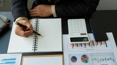 Finans müdürünün elleri masadaki, iş planındaki raporları analiz ediyor ve birçok grafiği dizüstü bilgisayar, hesap makinesi, kalem, üst görünüm ile analiz ediyor..