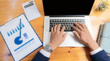 Finans müdürünün elleri masadaki, iş planındaki raporları analiz ediyor ve birçok grafiği dizüstü bilgisayar, hesap makinesi, kalem, üst görünüm ile analiz ediyor..