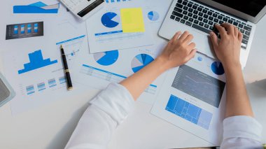 Finans müdürünün elleri masadaki, iş planındaki raporları analiz ediyor ve birçok grafiği dizüstü bilgisayar, hesap makinesi, kalem, üst görünüm ile analiz ediyor..