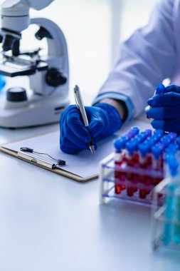 Atardamar kan örneğini inceleyen profesyonel bir doktor, mikroskopla hemşire araştırması laboratuvar laboratuarındaki kadın laboratuvar asistanının tuttuğu kan test tüpünü kapatın.