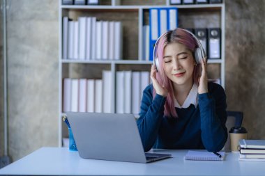 Kulaklık takan Asyalı bayan üniversite öğrencileri üniversite hazırlıkları için internette sörf yapmak için akıllı telefonlar ve dizüstü bilgisayarlar kullanıyorlar..
