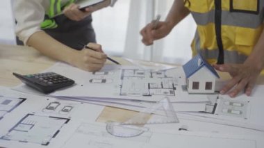 İnşaat ofisinde proje planı üzerinde çalışan mühendislerden oluşan bir ekip. İnşaat planının detaylarını açıklayan bir mimar.