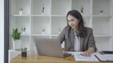 Asyalı iş kadını, dizüstü bilgisayar ve mali muhasebe grafikleriyle çalışırken stresli hissediyor. Ofiste çalışan genç bir kadın başını elinde tutmaktan yorulmuş ve başı ağrıyor.