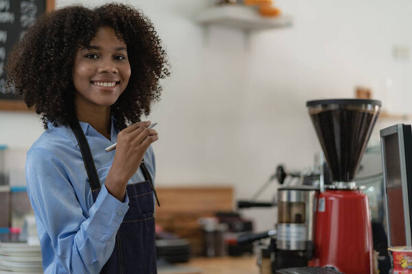Smiling african american barista standing behind the coffee shop counter accepting customers, food and drink concept
