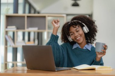 Not defterine dizüstü bilgisayarla yazı yazan Afrikalı Amerikalı bir kız. Çok çalışıyorum. İnternette çalışırken kulaklık takan bir kadın. Öğrenci kafede dil öğrenmek için heyecanlı.