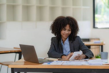 Genç mutlu başarılı iş kadını bilgisayarla çalışıyor ve analitik hesap makinesi ile ofisteki online toplantı konseptinde finansal grafik belgesi hesaplıyor.