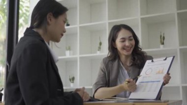 Belgede yer alan iki Asyalı iş kadını dosya analizi verilerini kullanarak ofis 4K 'da çalışan meslektaşlarıyla birlikte bir dizüstü bilgisayar oluşturuyorlar.