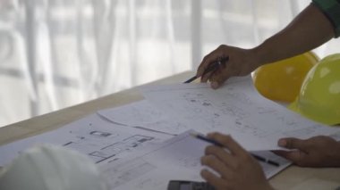 Team of 2 professional engineers in vests and helmets brainstorming plans in building and house construction project in 4k conference room.