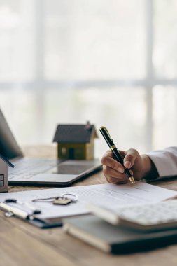 Real estate office, home sales agent sitting at desk with contract documents and house plans next to sale and rental concept.
