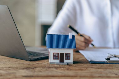 Real estate office, home sales agent sitting at desk with contract documents and house plans next to sale and rental concept.