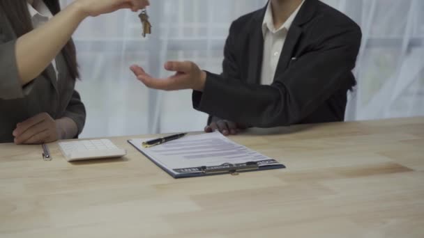 オフィス4Kでデスクでの最終取引後に新しい住宅所有者に手を振る販売代理店とキーを引き渡す — ストック動画