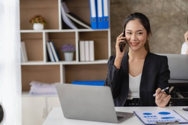 Asian businesswoman working on charts and graphs showing results in office with documents and laptop Worker documents calculating financial indicators, smiling and happy with success.