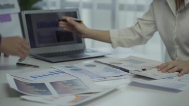 Group of Asian businessmen brainstorming close-up at plan meeting statistical analysis and pointing graph employee taking notes with laptop on table finance business success statistics concept