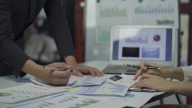 Group of Asian businessmen brainstorming close-up at plan meeting statistical analysis and pointing graph employee taking notes with laptop on table finance business success statistics concept