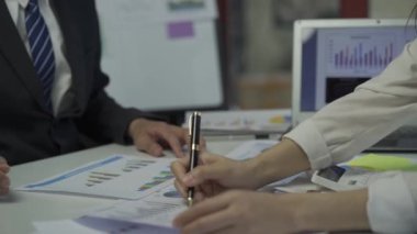 Group of Asian businessmen brainstorming close-up at plan meeting statistical analysis and pointing graph employee taking notes with laptop on table finance business success statistics concept
