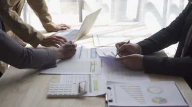Group of Asian businessmen brainstorming close-up at plan meeting statistical analysis and pointing graph employee taking notes with laptop on table finance business success statistics concept