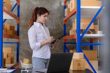Young Asian woman checking parcels for delivery taking orders with small business laptop. SME business owners check orders online Prepare to pack products for sale to customers, SME business ideas