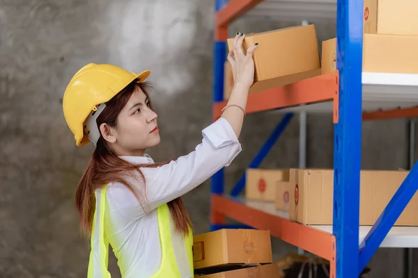 Customs warehouse worker with laptop phone Inspection of the goods of the Customs Department Young woman in yellow vest and hat checking boxes on blurred storage shelf
